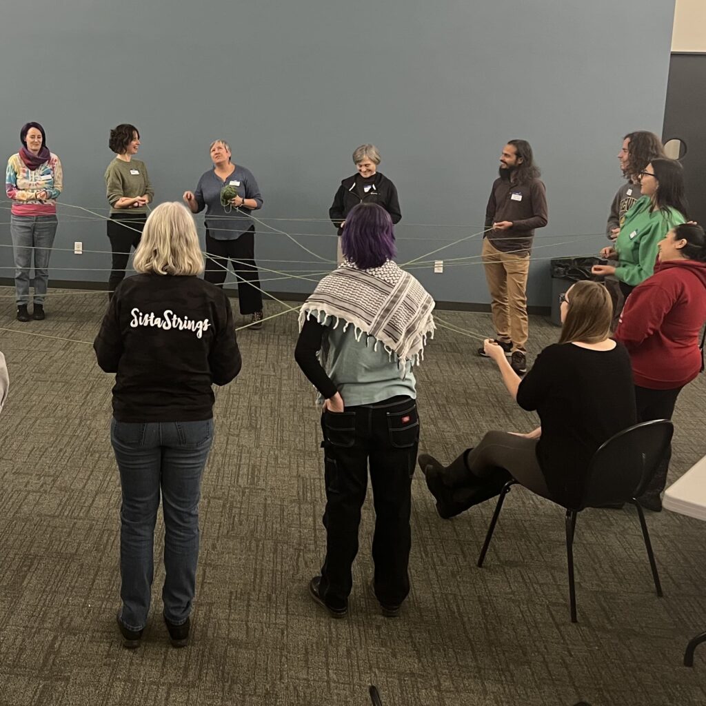 Community members at a Fair Future Meetup gathered around in a circle participating in a community building activity with yarn.